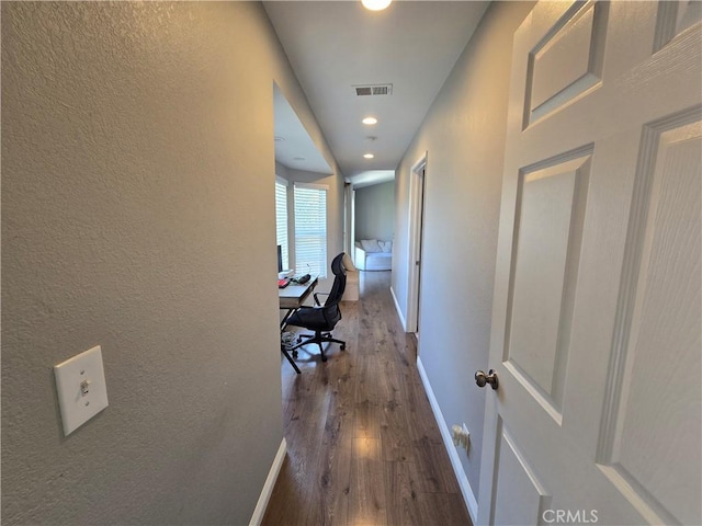hall featuring baseboards, visible vents, a textured wall, and dark wood-type flooring