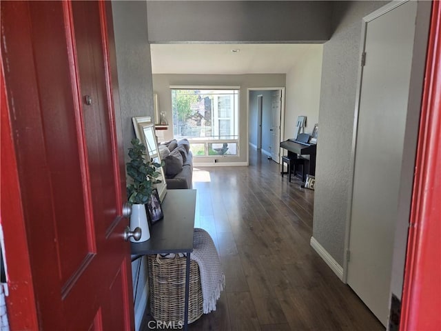 corridor with baseboards, a textured wall, and dark wood-type flooring