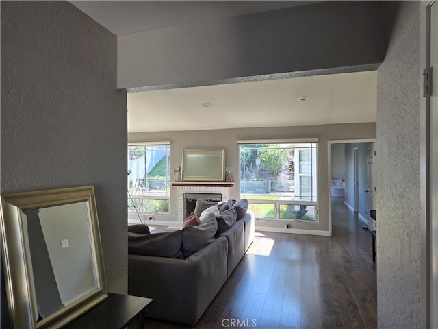 living room featuring a fireplace, a textured wall, dark wood-style flooring, and plenty of natural light