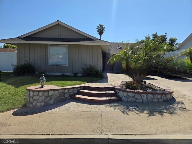 view of front of property with board and batten siding, a front lawn, and fence