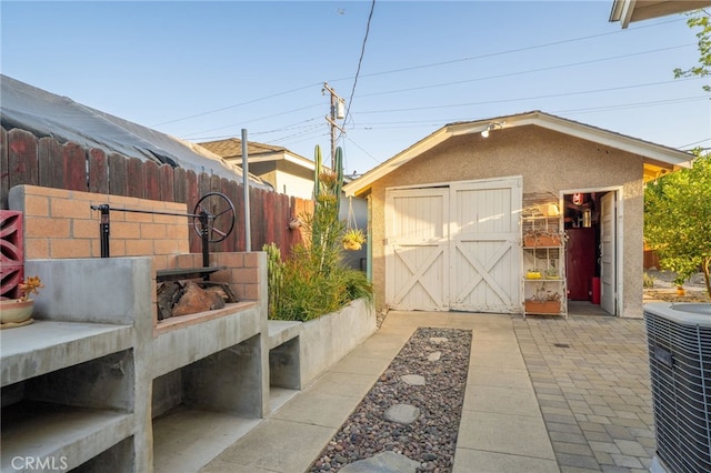view of patio featuring an outdoor structure, a storage unit, central AC, and fence