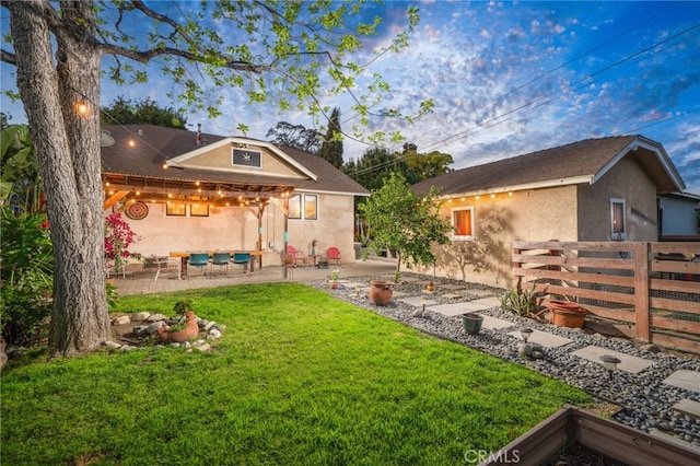 rear view of property featuring fence, a patio area, a yard, and stucco siding