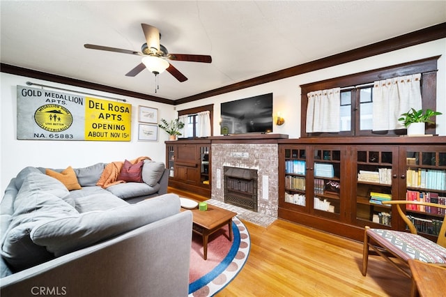 living area featuring wood finished floors, ornamental molding, a tile fireplace, and ceiling fan