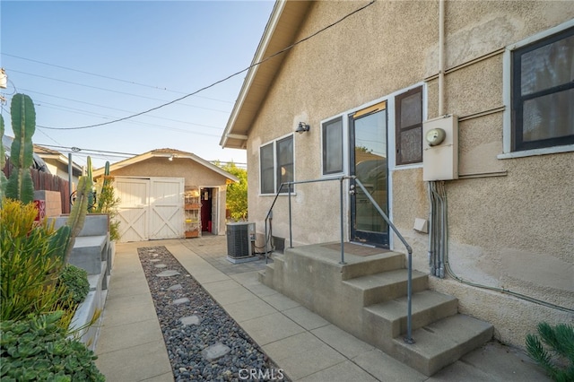 view of home's exterior with a storage unit, an outdoor structure, central AC, and stucco siding