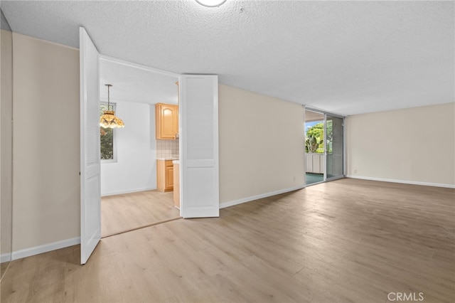 unfurnished living room featuring baseboards, light wood finished floors, and a textured ceiling