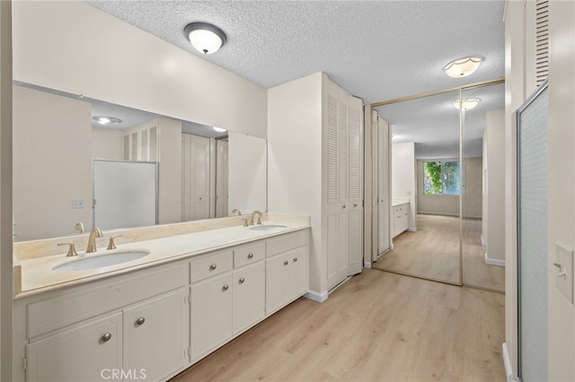 bathroom with double vanity, a sink, a textured ceiling, and wood finished floors
