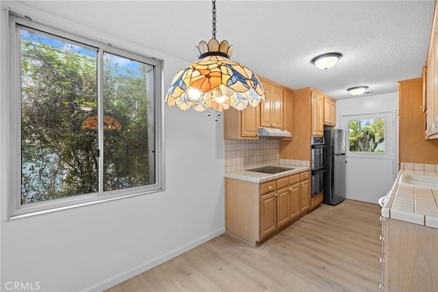 kitchen with freestanding refrigerator, tile countertops, under cabinet range hood, and light wood-style floors