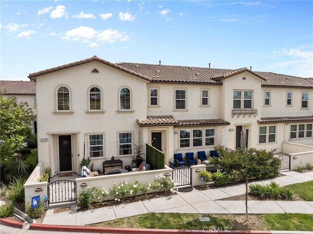 mediterranean / spanish house with a fenced front yard, stucco siding, a tiled roof, and a gate