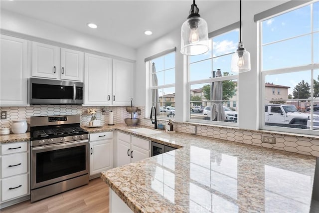 kitchen featuring decorative backsplash, light wood-style floors, appliances with stainless steel finishes, white cabinets, and a sink