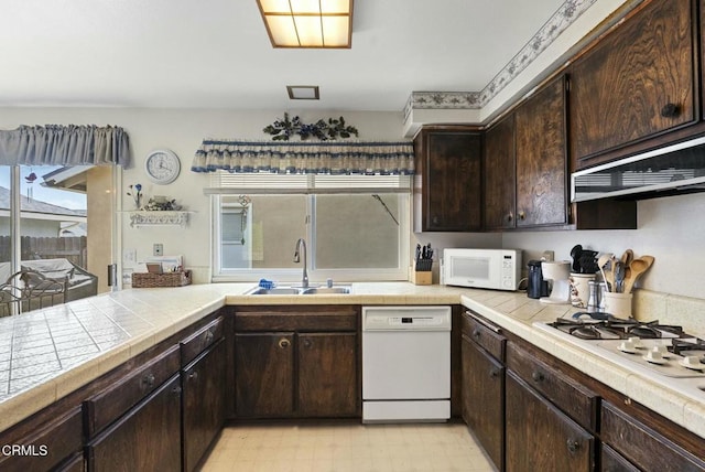 kitchen featuring dark brown cabinets, white appliances, tile counters, and a sink