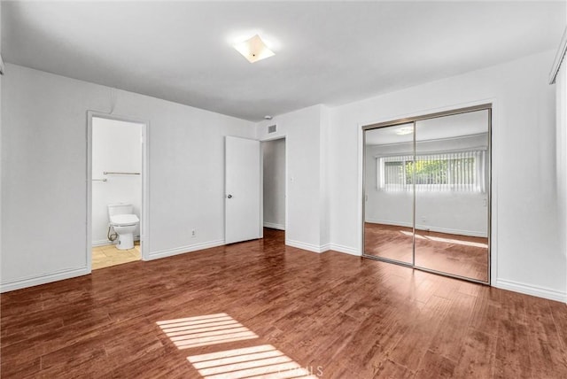 unfurnished bedroom with wood finished floors, visible vents, connected bathroom, a closet, and baseboards