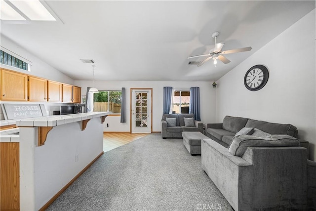living area with visible vents, baseboards, ceiling fan, light colored carpet, and vaulted ceiling