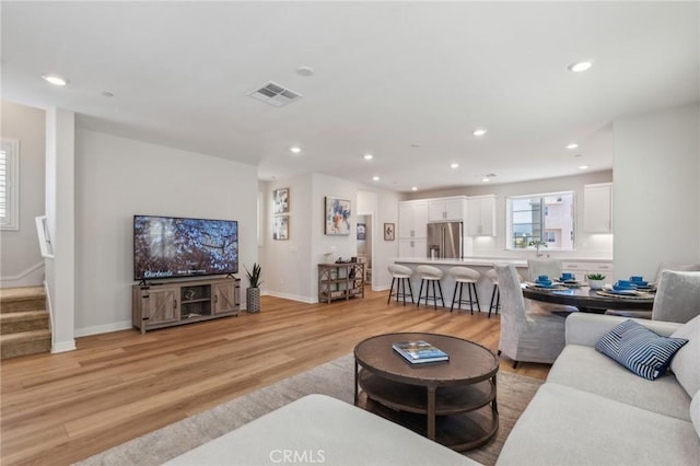 living area featuring recessed lighting, visible vents, baseboards, light wood-style flooring, and stairs