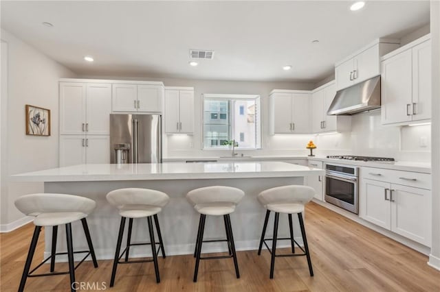 kitchen with a sink, under cabinet range hood, stainless steel appliances, white cabinetry, and a kitchen island