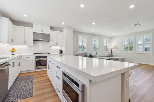 kitchen with a kitchen island, stainless steel appliances, under cabinet range hood, visible vents, and recessed lighting