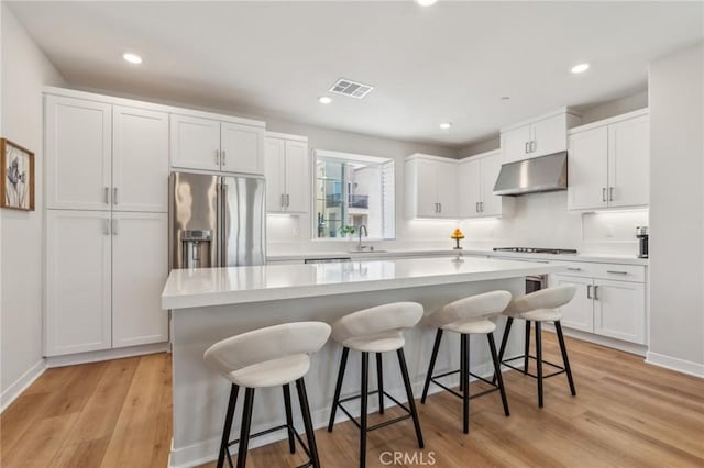 kitchen with high end refrigerator, a sink, a breakfast bar, white cabinets, and under cabinet range hood