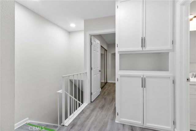 hall featuring an upstairs landing, light wood-style flooring, baseboards, and recessed lighting