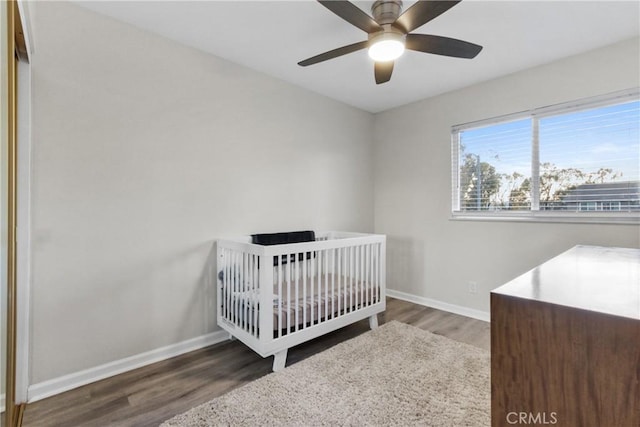 bedroom with baseboards, wood finished floors, a nursery area, and ceiling fan