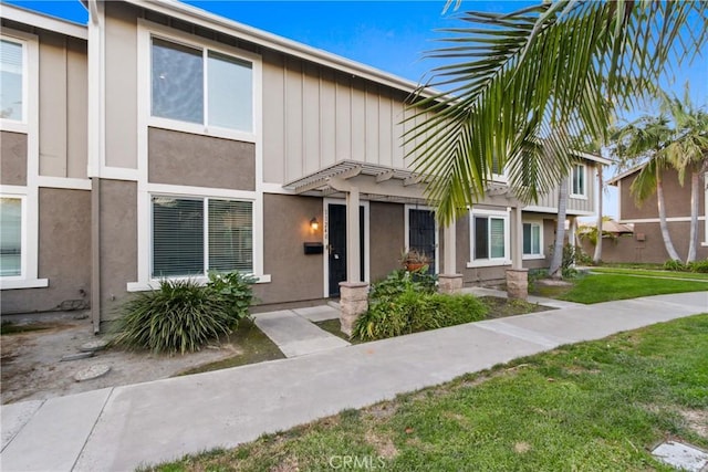 view of property featuring a front lawn, stucco siding, and board and batten siding