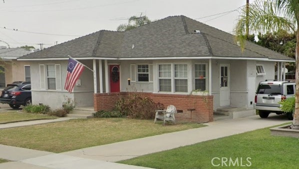 view of front of property featuring stucco siding, a front lawn, brick siding, and a shingled roof