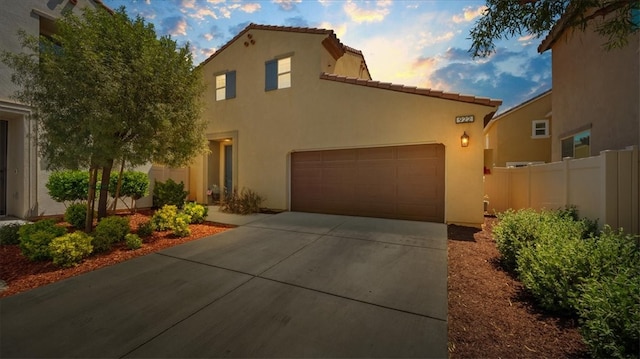 mediterranean / spanish-style home with a garage, fence, stucco siding, concrete driveway, and a tile roof