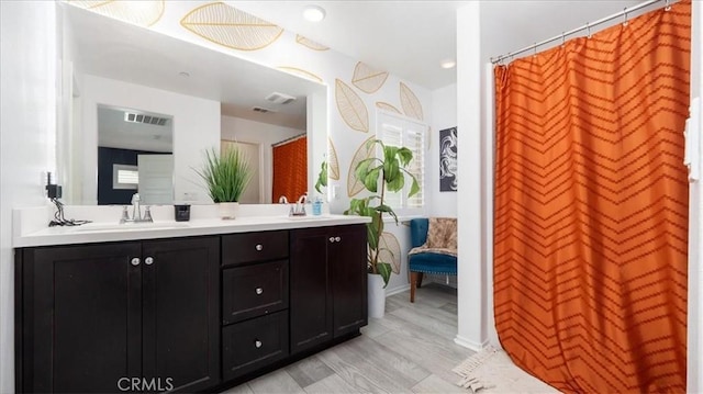 ensuite bathroom featuring double vanity, visible vents, wood finished floors, a sink, and ensuite bath
