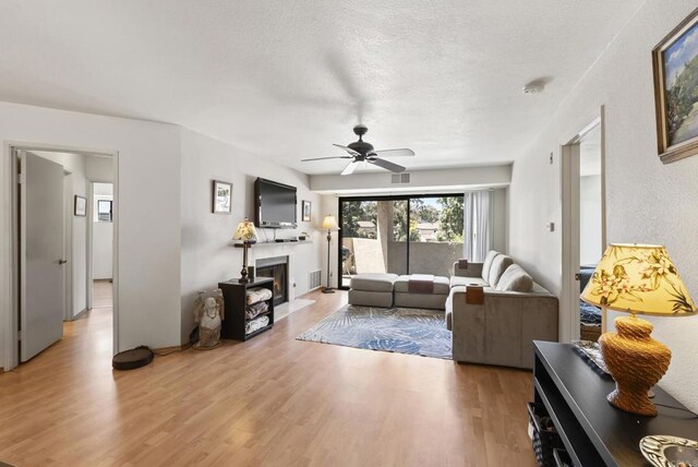 9725 Mesa Springs Way Unit 176, San Diego, CA 92126 - living room featuring light wood finished floors, a fireplace with flush hearth, a ceiling fan, and a textured ceiling