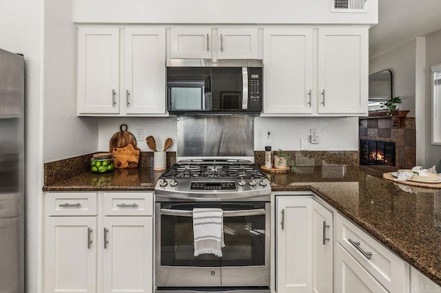 720 San Luis Obispo Pl Unit D, San Diego, CA 92109 - kitchen with stainless steel appliances, dark stone counters, a tiled fireplace, visible vents, and white cabinetry