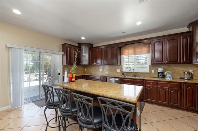 kitchen with light tile patterned flooring, light stone counters, a sink, and dishwasher