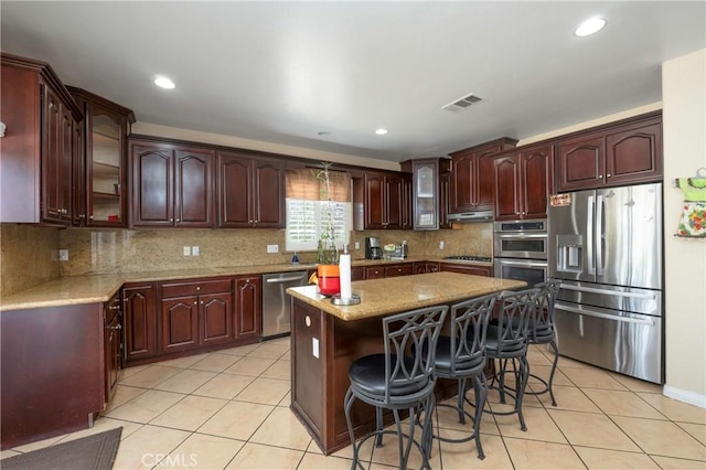 kitchen featuring visible vents, appliances with stainless steel finishes, glass insert cabinets, under cabinet range hood, and light tile patterned flooring