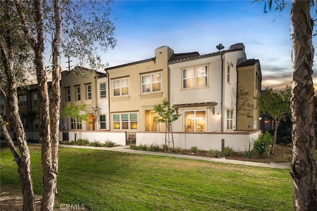 back of property featuring a lawn, stucco siding, and a tiled roof