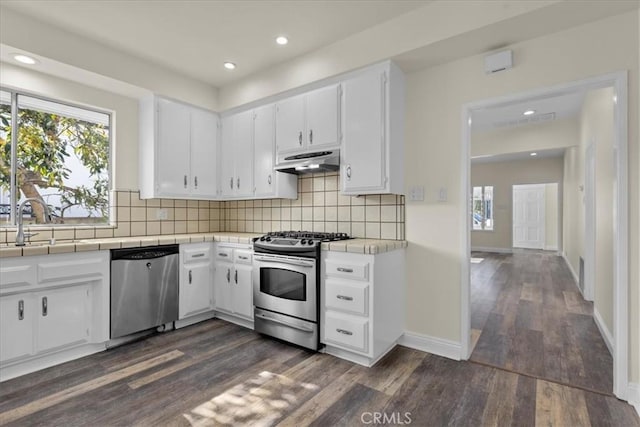 kitchen with dark wood-style flooring, tasteful backsplash, tile countertops, appliances with stainless steel finishes, and under cabinet range hood