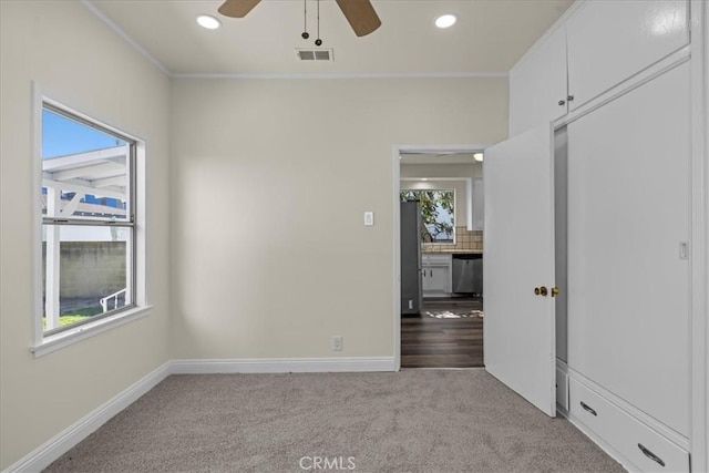 carpeted empty room featuring ornamental molding, baseboards, a ceiling fan, and visible vents