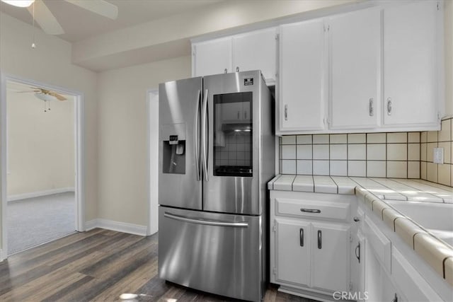 kitchen with tile counters, ceiling fan, stainless steel fridge with ice dispenser, decorative backsplash, and white cabinetry
