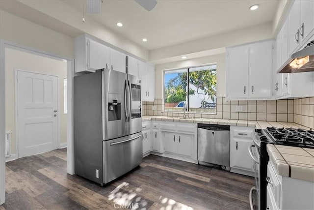 kitchen with tile counters, recessed lighting, under cabinet range hood, dark wood-type flooring, and appliances with stainless steel finishes