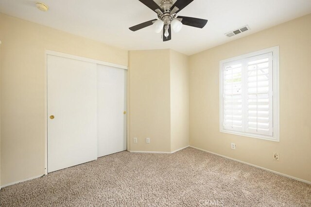unfurnished bedroom featuring carpet flooring, baseboards, visible vents, a ceiling fan, and a closet