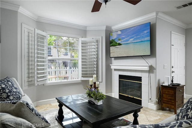 living area with a tile fireplace, crown molding, a ceiling fan, visible vents, and baseboards