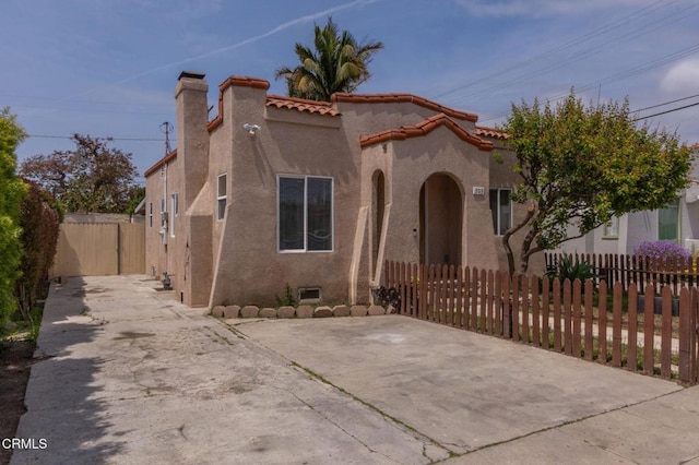 mediterranean / spanish house featuring a tiled roof, a chimney, fence private yard, concrete driveway, and stucco siding