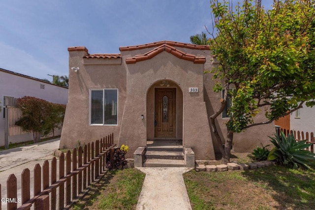 view of exterior entry featuring stucco siding, fence, and a tiled roof