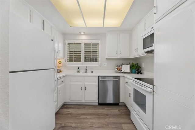 kitchen with wood finished floors, white cabinetry, a sink, and white appliances