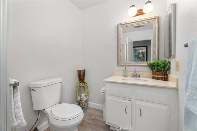 bathroom featuring wood finished floors, vanity, baseboards, toilet, and visible vents