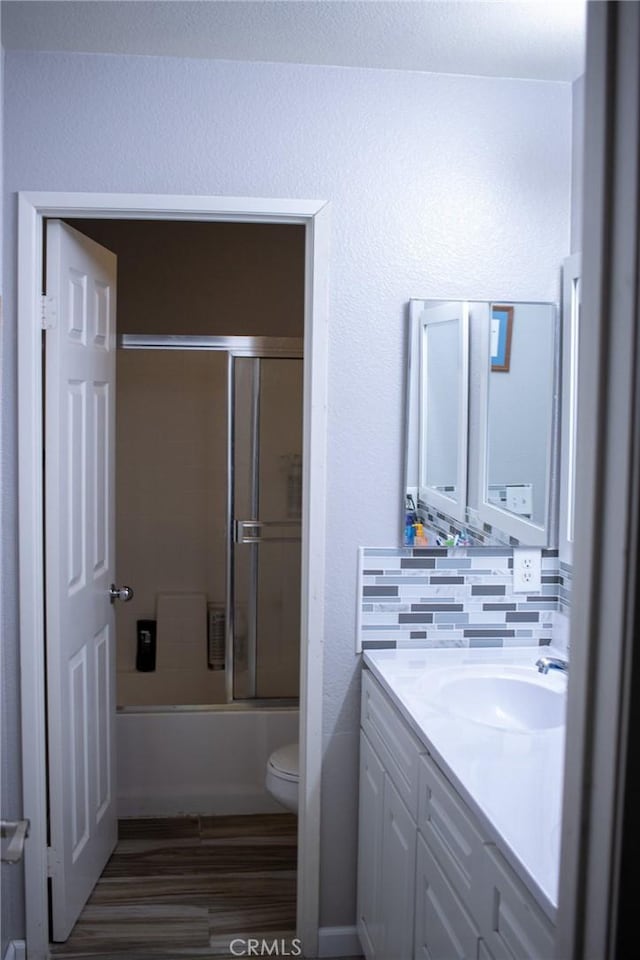 bathroom with vanity, wood finished floors, toilet, tasteful backsplash, and enclosed tub / shower combo
