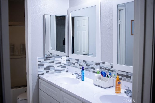 bathroom with backsplash, toilet, a sink, and double vanity