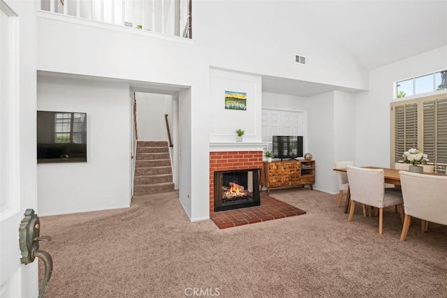 living room with a brick fireplace, high vaulted ceiling, carpet, visible vents, and stairway