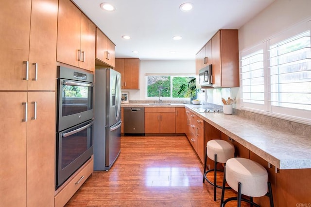 kitchen with appliances with stainless steel finishes, a sink, light wood finished floors, light countertops, and a kitchen breakfast bar