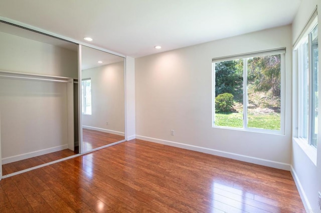 unfurnished bedroom with multiple windows, hardwood / wood-style flooring, baseboards, a closet, and recessed lighting