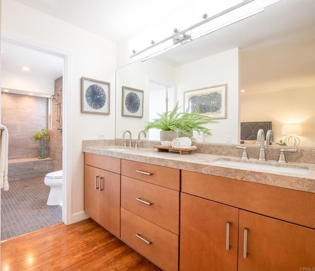 bathroom featuring toilet, a tile shower, double vanity, and wood finished floors