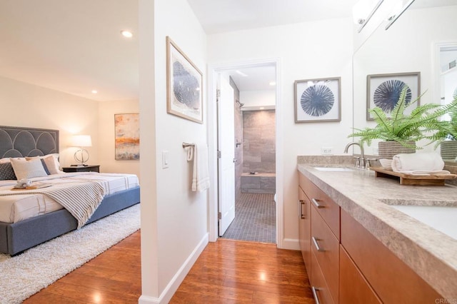 bathroom with hardwood / wood-style flooring, a shower, recessed lighting, double vanity, and baseboards