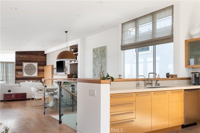 kitchen featuring wood finished floors, light countertops, a sink, dishwasher, and hanging light fixtures