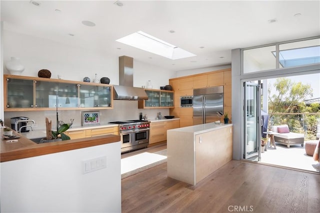 kitchen featuring exhaust hood, built in appliances, light wood-style flooring, a peninsula, and a skylight
